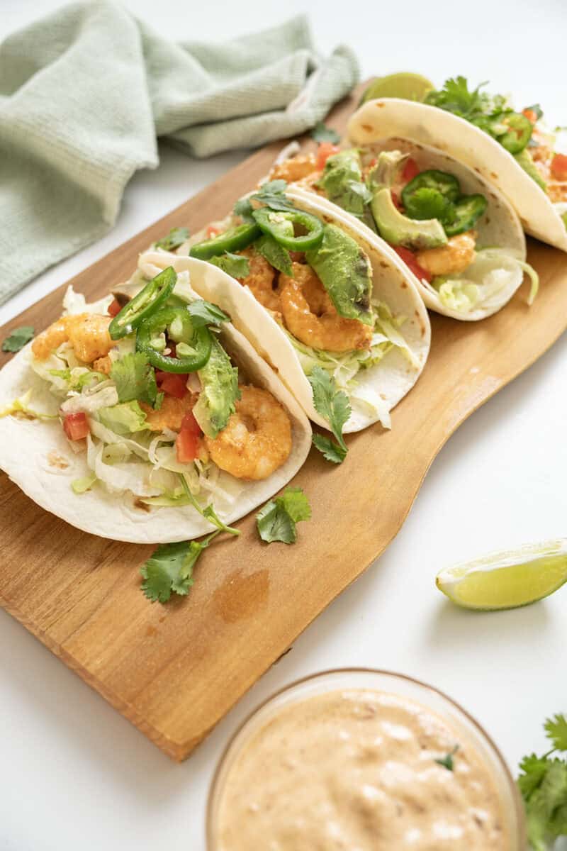 Volcano shrimp tacos on a cutting board topped with cilantro, tomatoes, jalapeno, and avocado.
