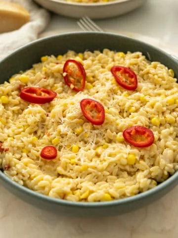 Creamy corn orzo in a bowl topped with red fresno peppers.
