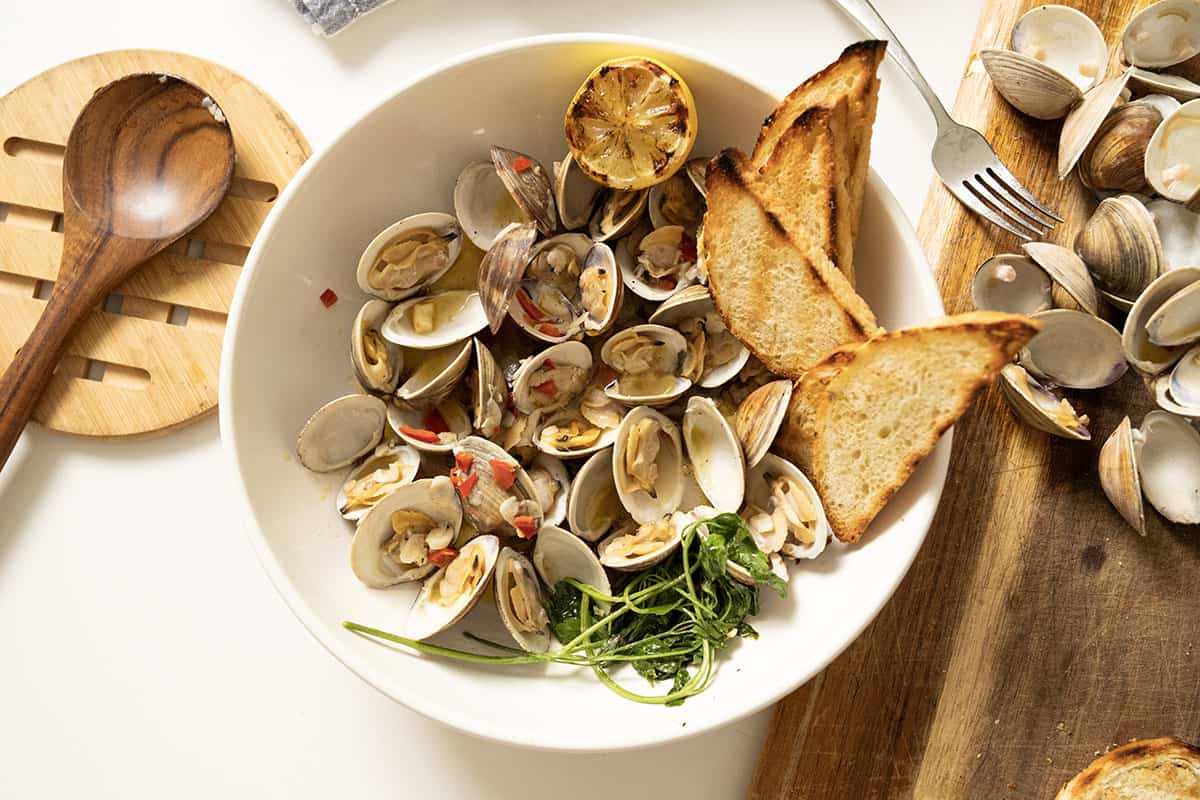 Grilled clams with white wine sauce in a bowl with toasted semolina bread.