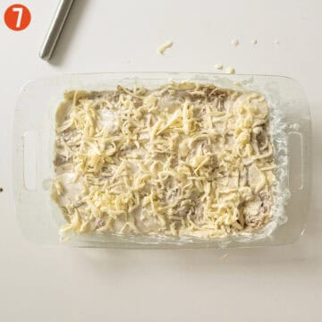 Pressing the potato mixture into a baking dish and topping with cheese.