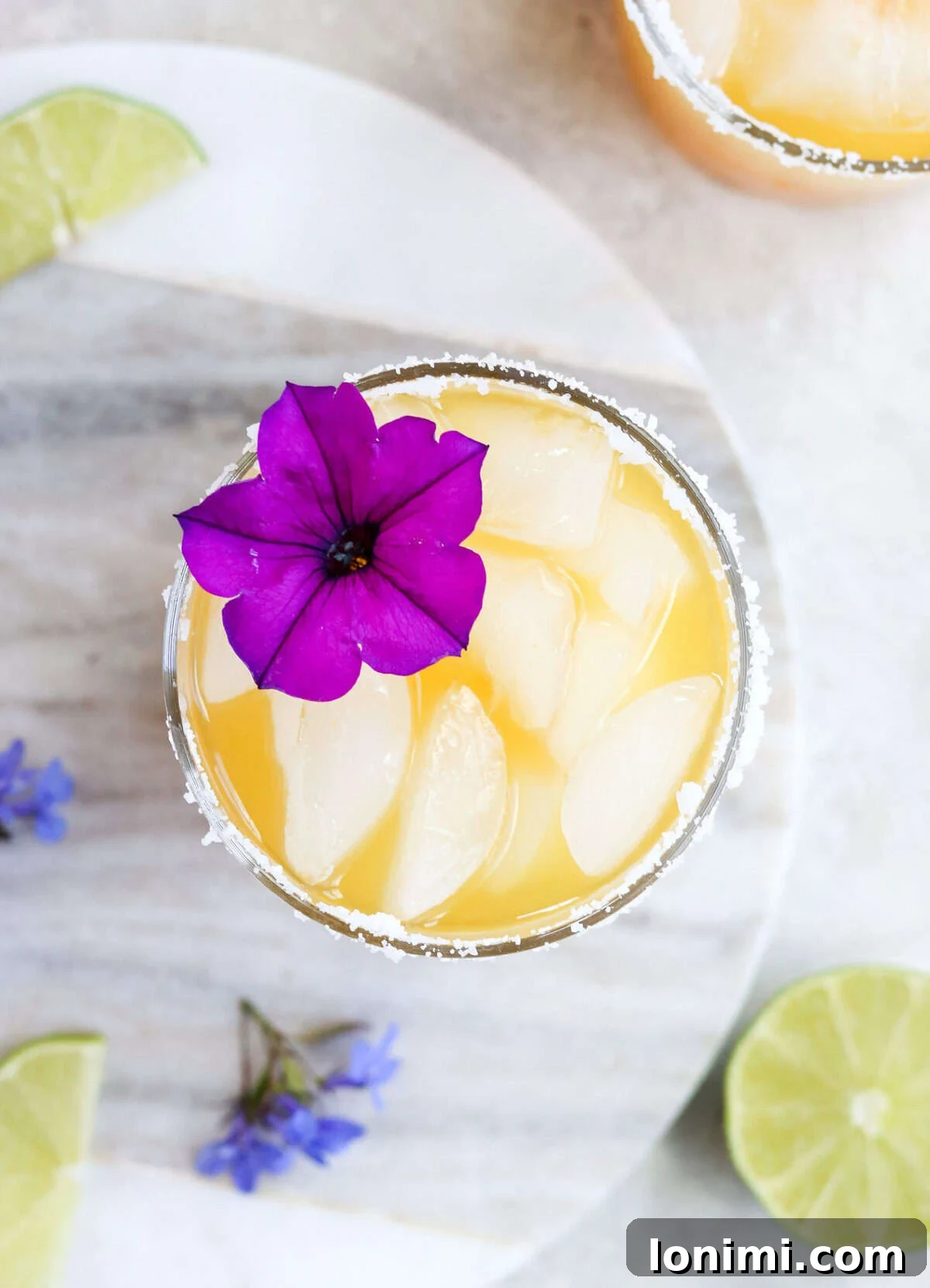 An overhead view of a beautifully garnished passion fruit margarita, featuring a vibrant purple tropical flower and a lime wedge.