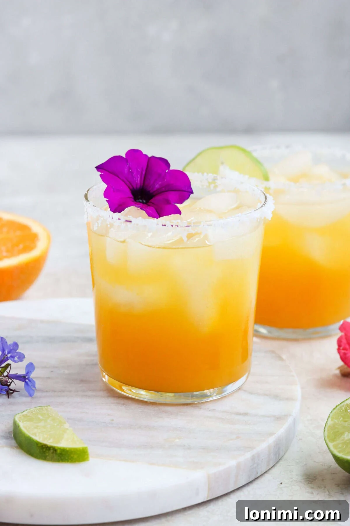 A close-up shot of two glasses filled with sparkling passion fruit margaritas, each elegantly garnished with a delicate purple flower.