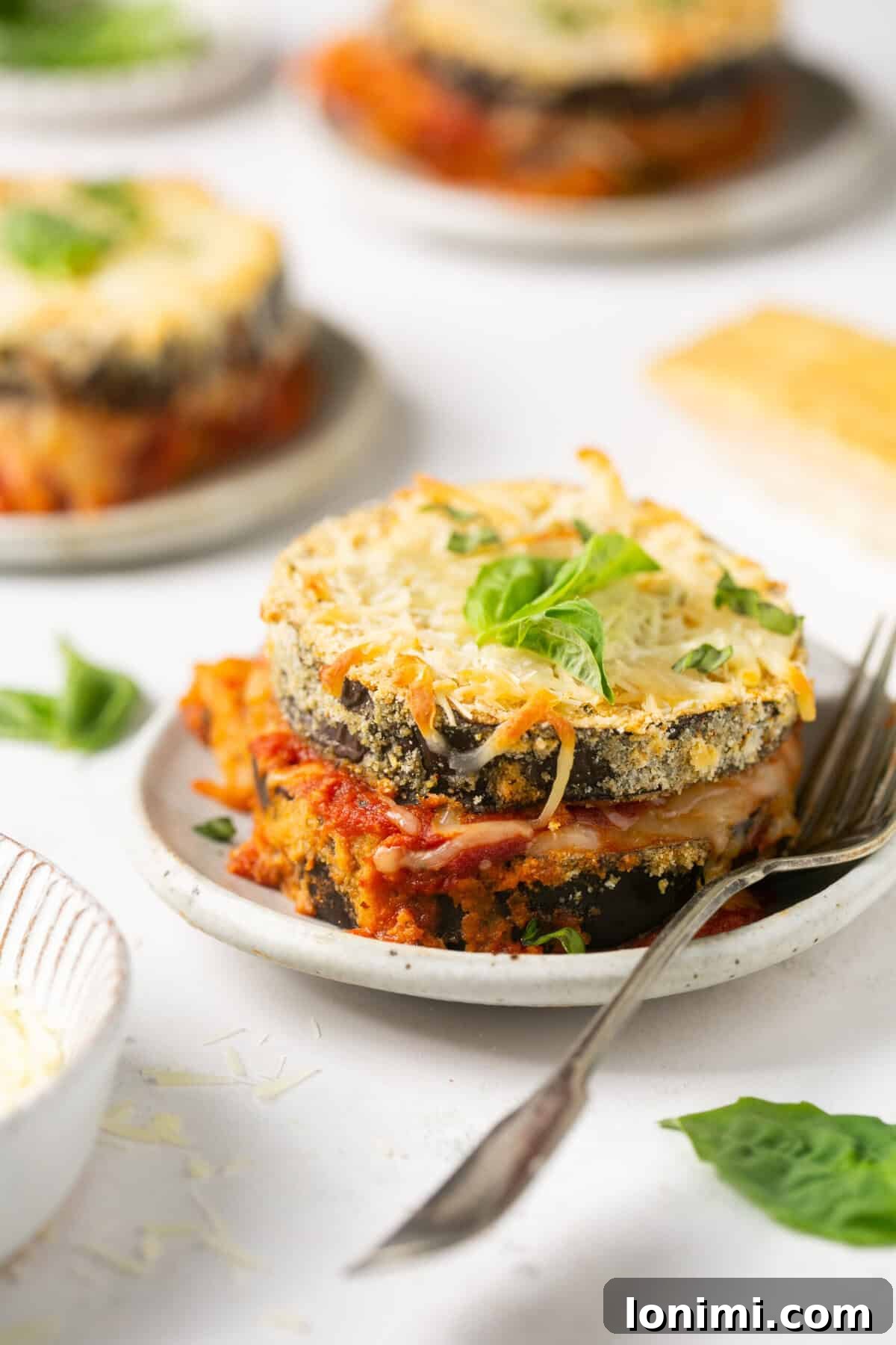 3 individual servings of keto eggplant parmesan on white plates with a silver fork