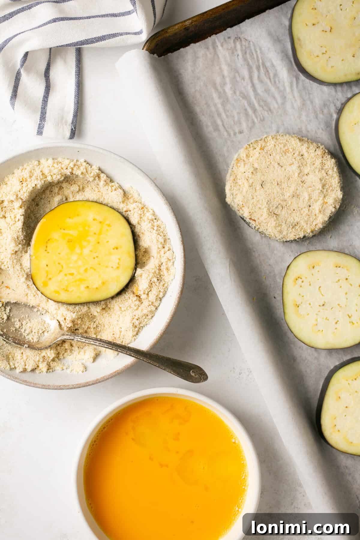 dipping eggplant rounds in egg wash and then an almond flour mixture and placing them on a sheet pan