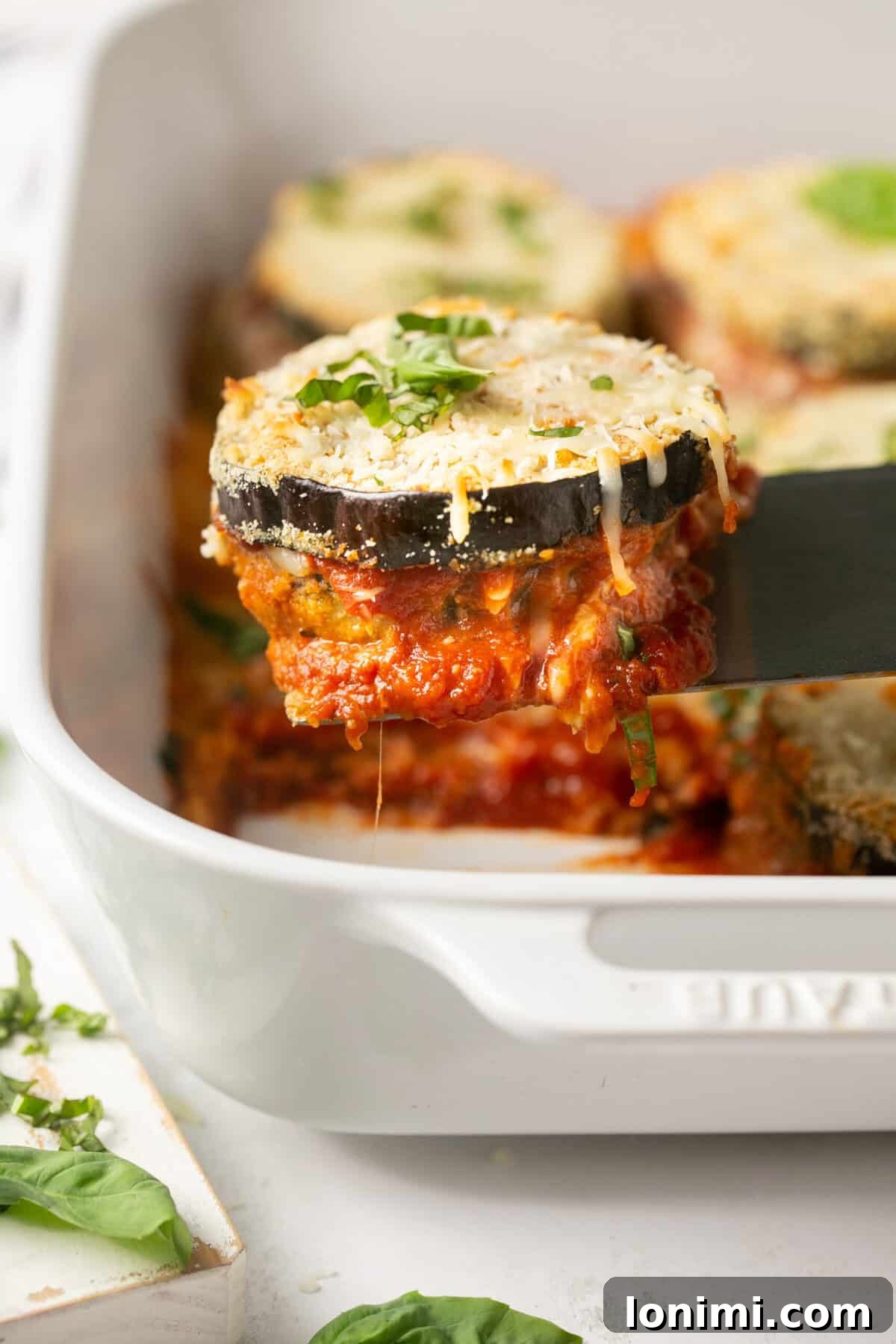A slice of eggplant parmesan being lifted out of a casserole dish by a spatula