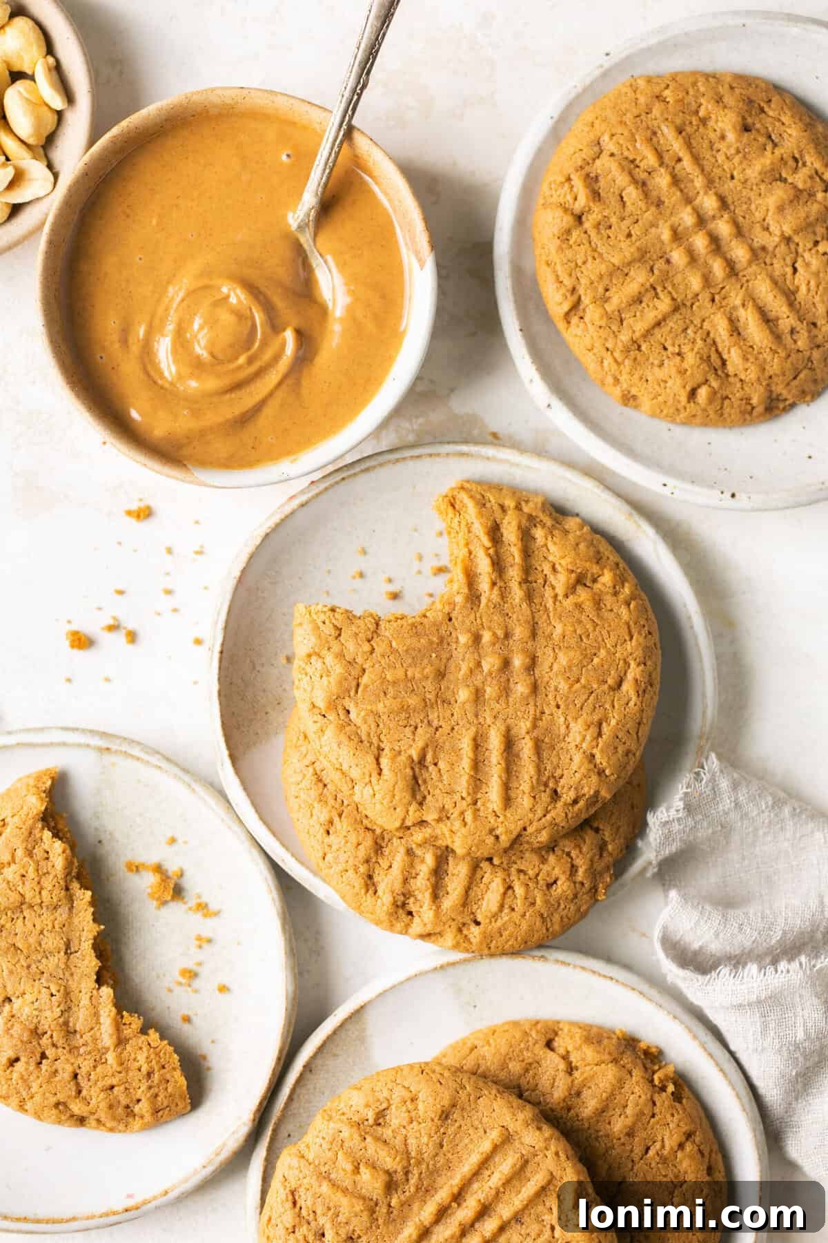 Mary's Signature Gluten-Free Peanut Butter Cookies 2 Freshly baked gluten-free peanut butter cookies displayed on small white plates, accompanied by a bowl of creamy peanut butter and a white napkin, highlighting their golden-brown perfection.