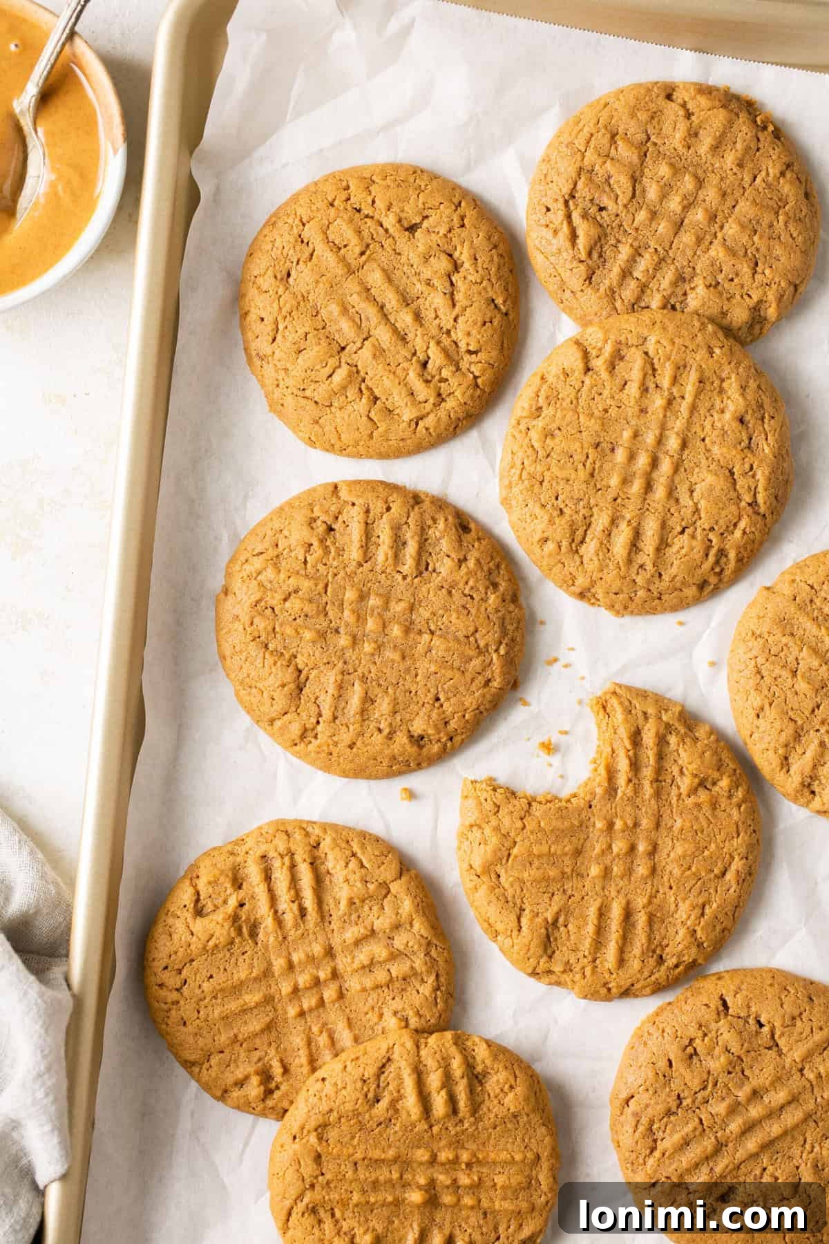 Mary's Signature Gluten-Free Peanut Butter Cookies 6 A baking sheet lined with parchment paper, showcasing freshly baked gluten-free peanut butter cookies neatly arranged, golden and ready to cool.
