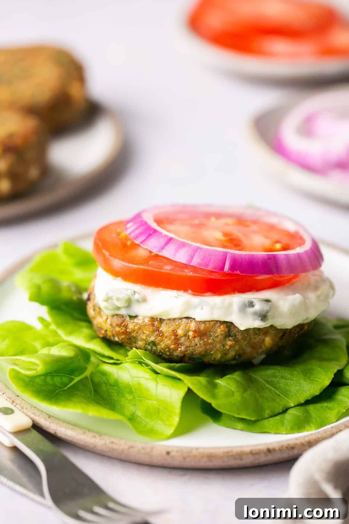 Flavorful Air-Fried Turkey Burgers with Spinach and Feta 6 A delicious air fryer turkey burger served on a lettuce leaf, garnished with tomato, red onion, and a drizzle of homemade tzatziki sauce.