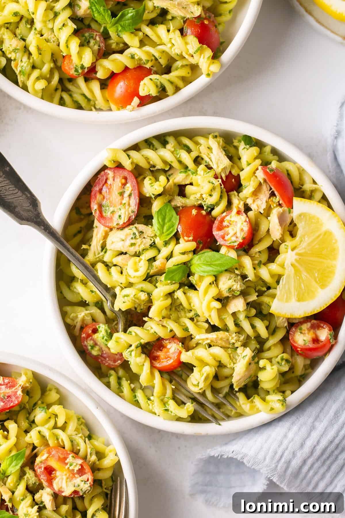 a closeup shot of three white bowls filled with pesto pasta and tomatoes.
