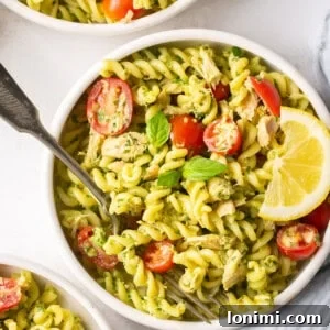 dairy free pesto tuna pasta in a bowl with tomatoes, basil, and a slice of lemon