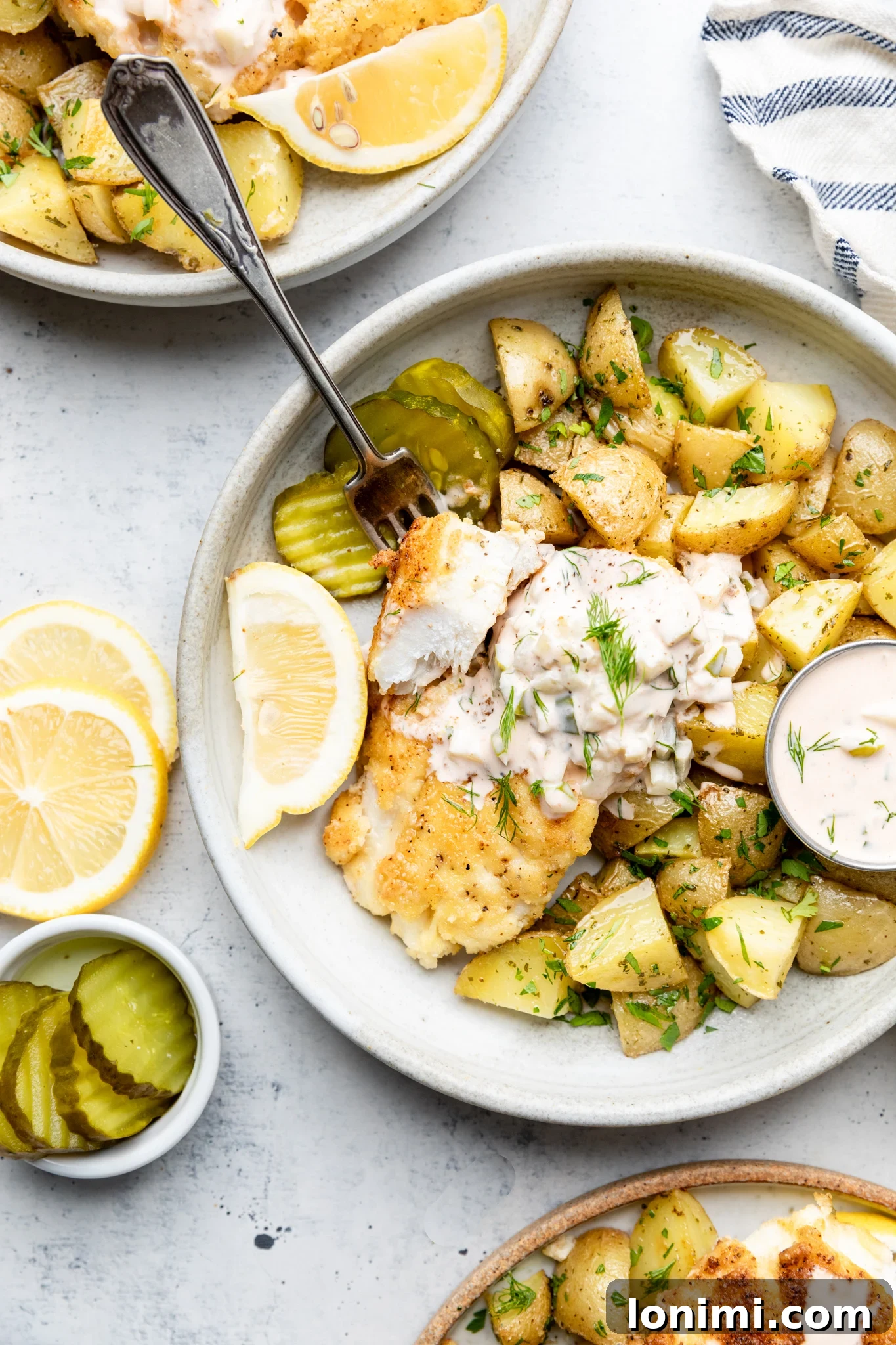Gluten Free Fish and Chips with potatoes, tartar sauce, and lemon and pickles in a bowl