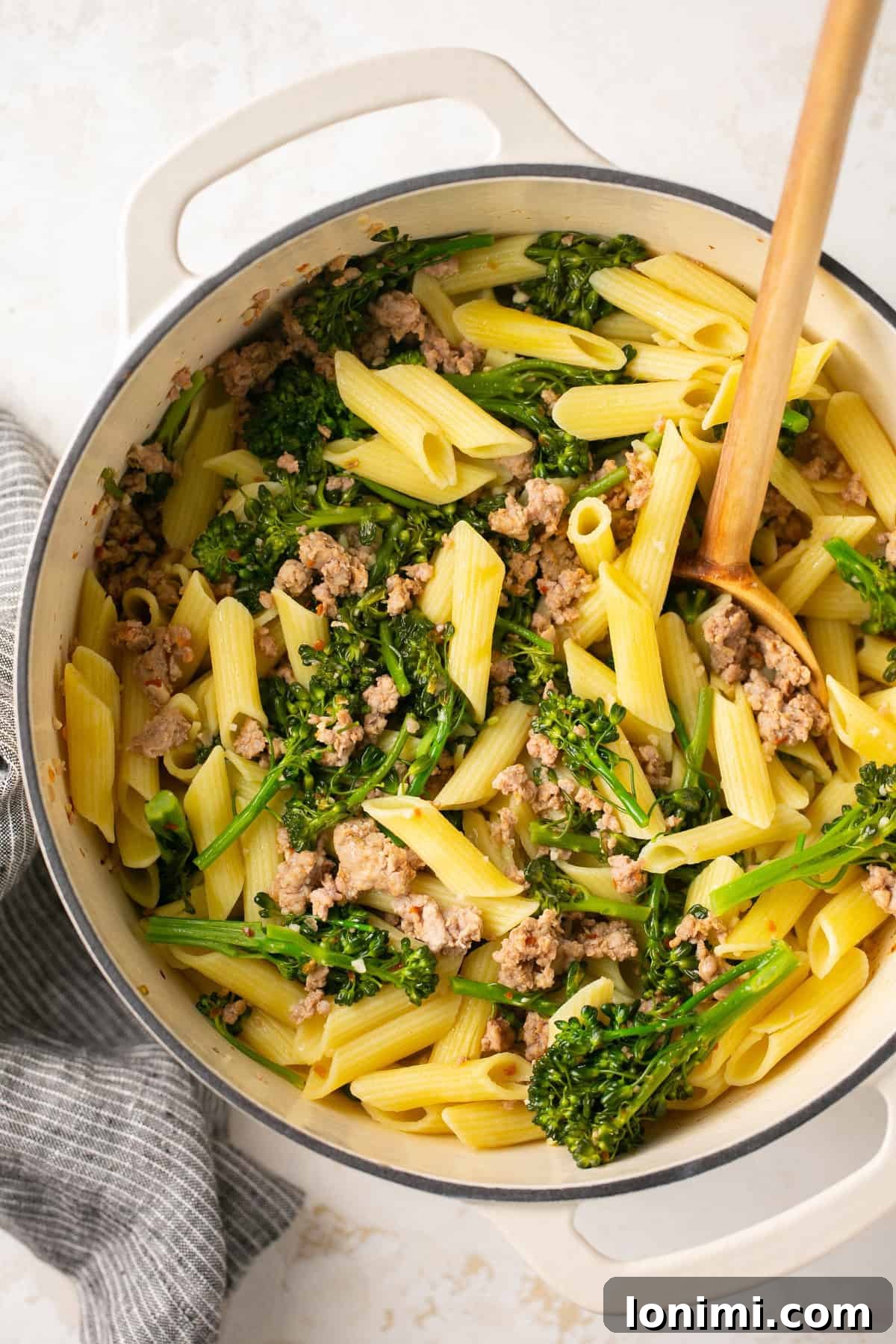 A white Dutch oven filled with freshly cooked sausage broccolini pasta.