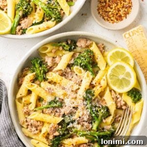 sausage broccolini pasta with penne in 2 white bowls with a nesting bowl full of crushed red pepper