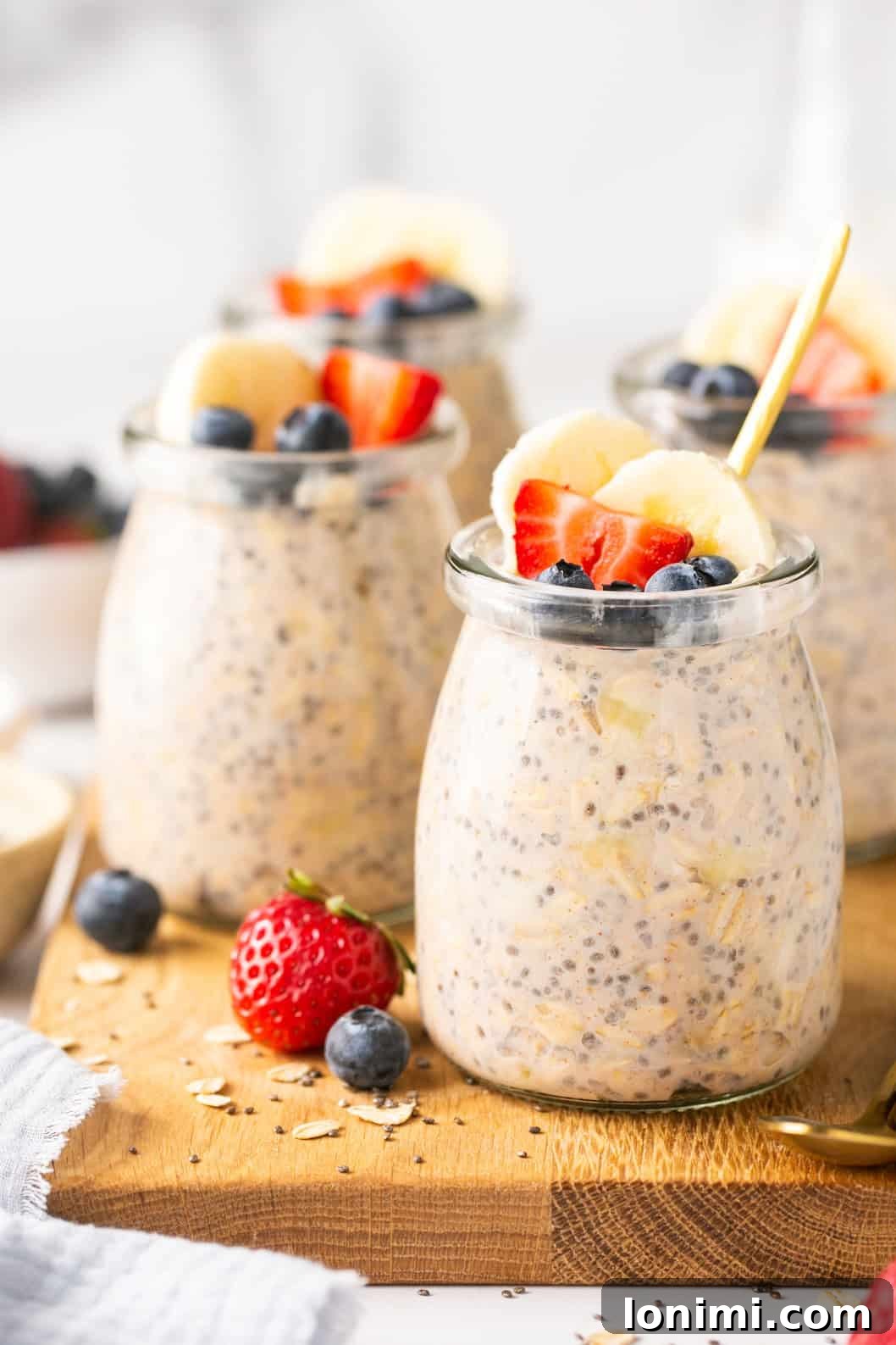 overnight oats in small jars topped with fruit on a wooden cutting board