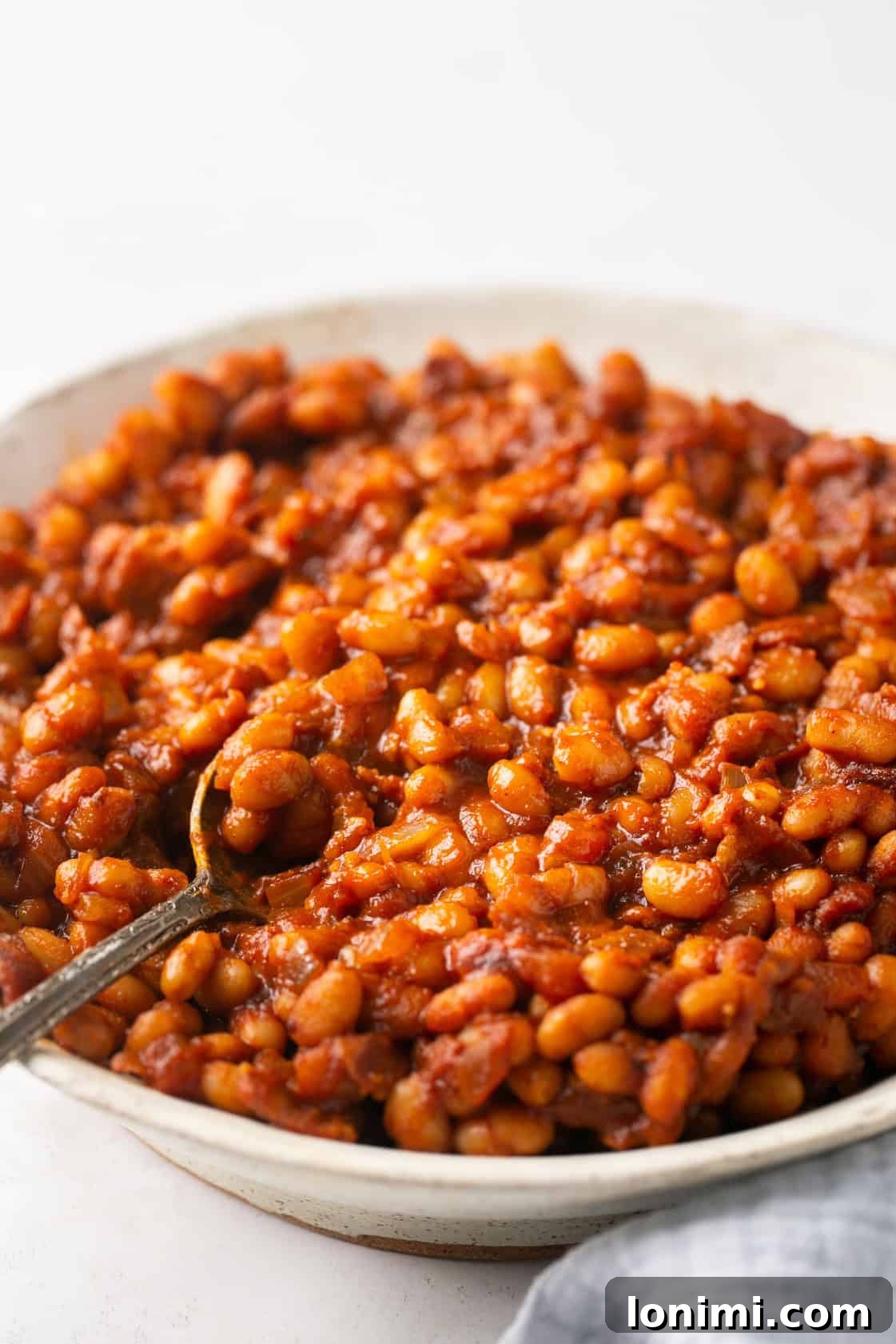 Nutritious Bean Bake 2 A bowl of healthy baked beans with a silver spoon, ready to be enjoyed as a perfect side dish.