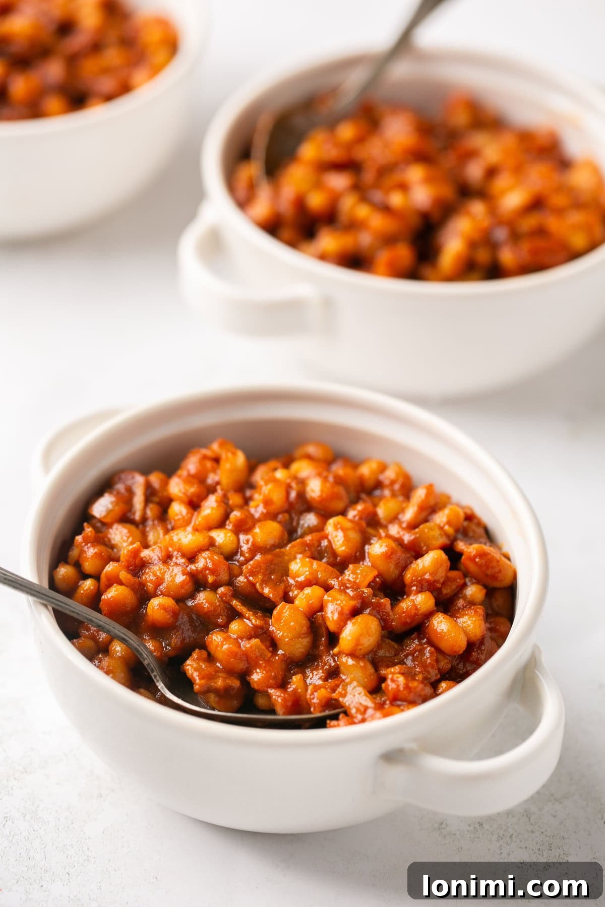 Nutritious Bean Bake 6 Two small white bowls filled with healthy baked beans, garnished with fresh herbs and silver spoons.