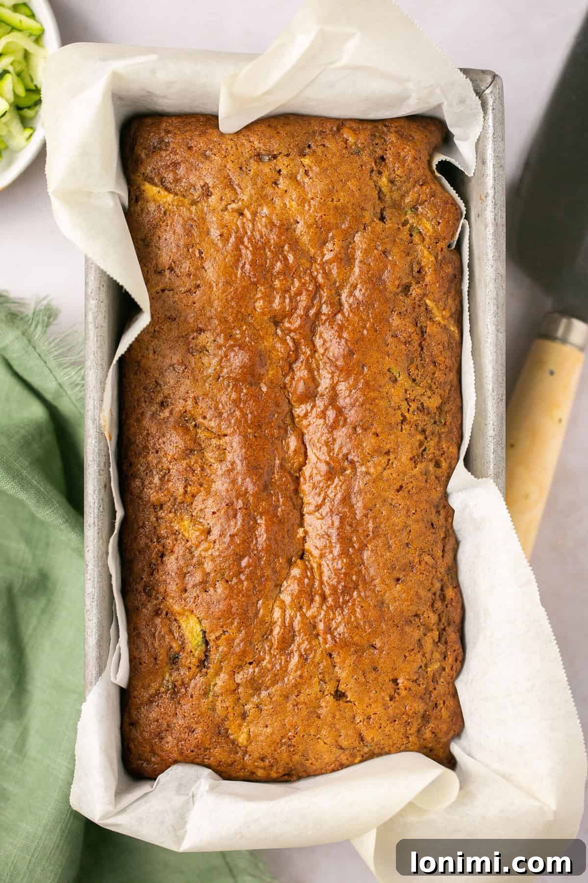 A freshly baked loaf of gluten free zucchini bread, still warm in a metal loaf pan lined with parchment paper, ready to be cooled.
