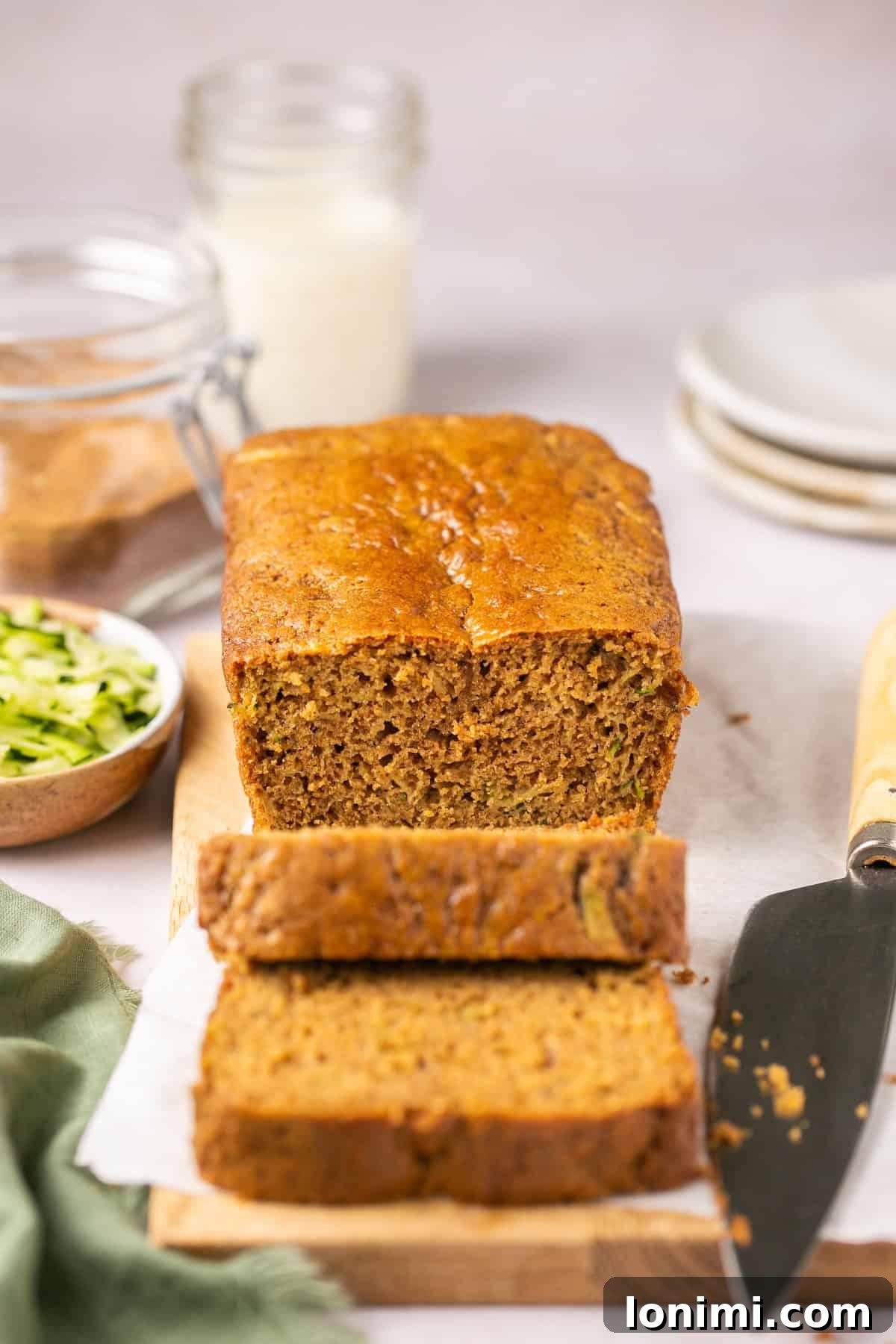 Two enticing slices of gluten-free zucchini bread placed in front of a half-eaten loaf on a rustic wooden cutting board, inviting a taste.