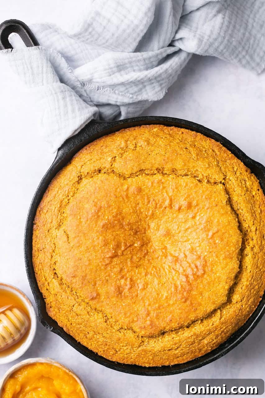 Golden Sweet Potato Cornbread 6 A whole baked sweet potato cornbread, perfectly golden and sliced, rests in a cast iron pan next to a small bowl of glistening honey, inviting a sweet drizzle.