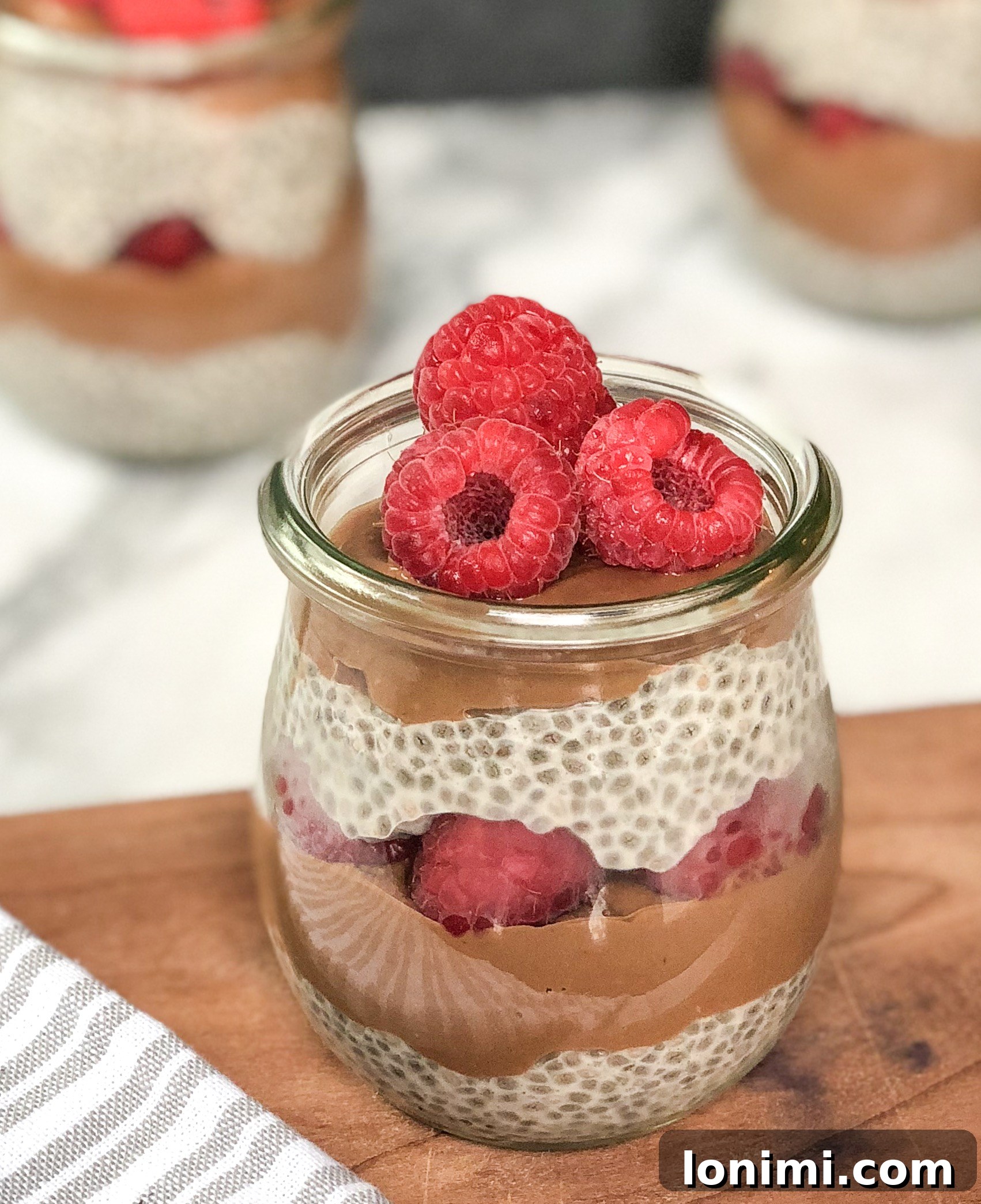Choco Berry Chia Dream 2 Beautifully layered Chocolate Raspberry Chia Parfaits in glass jars, showcasing the cinnamon chia pudding, rich chocolate avocado mousse, and vibrant raspberries, ready to be enjoyed.