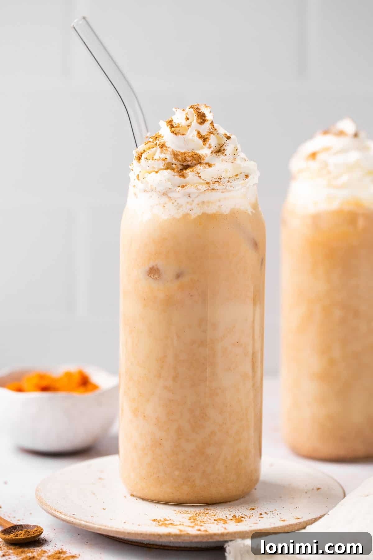a closeup photo of an iced pumpkin spiced latte topped with whipped cream in a glass cup with a clear straw
