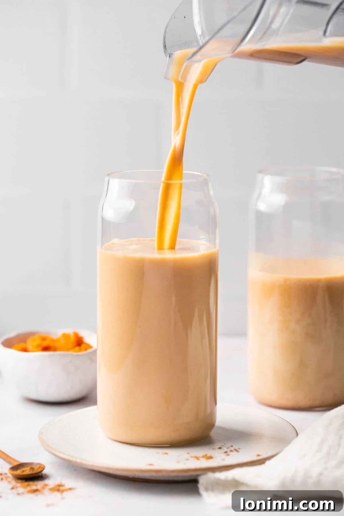 a pitcher pouring iced pumpkin spiced latte ingredients into a glass cup. 