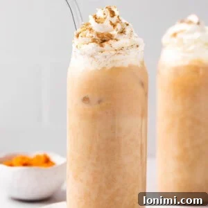 iced pumpkin spiced latte in a glass topped with whipped cream with a glass straw