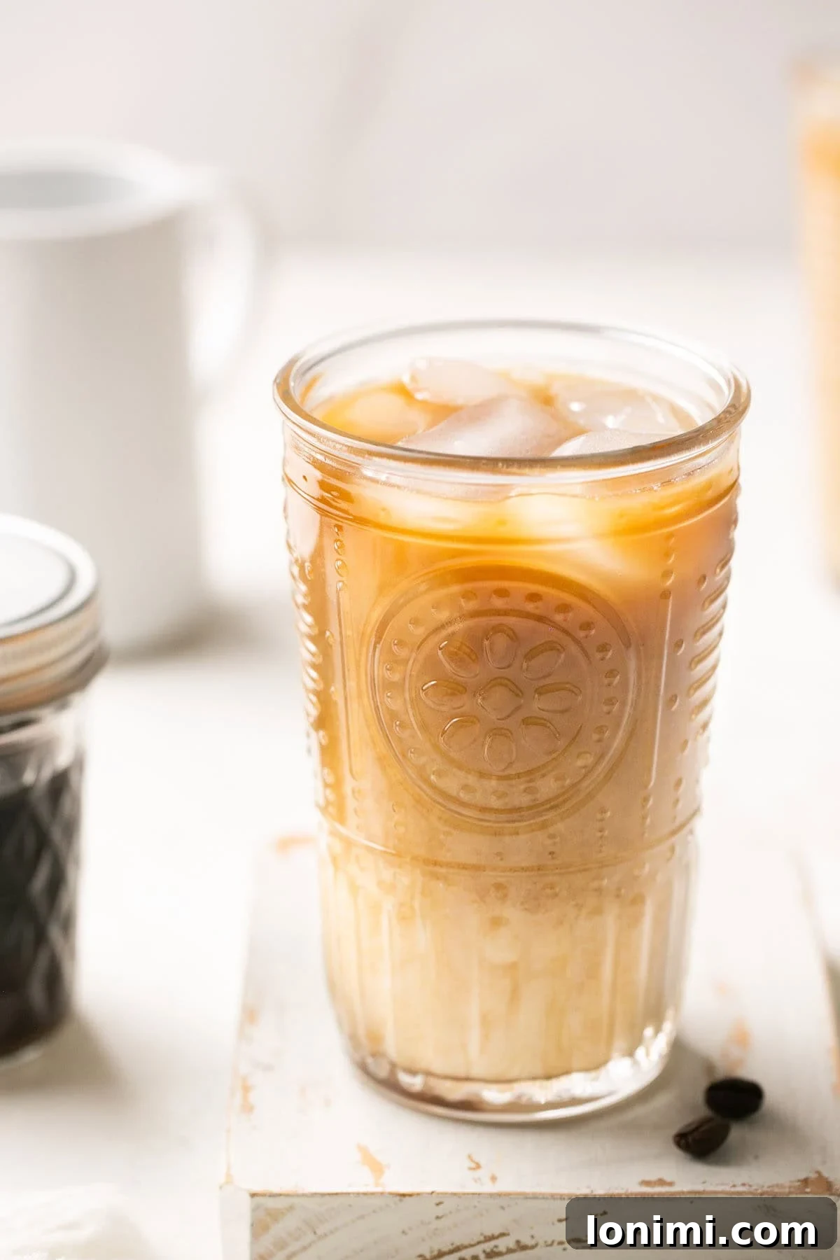 A vibrant close-up of a glass of shaken espresso with oat milk and ice, positioned next to a jar of brown sugar syrup, highlighting the key components of the drink.