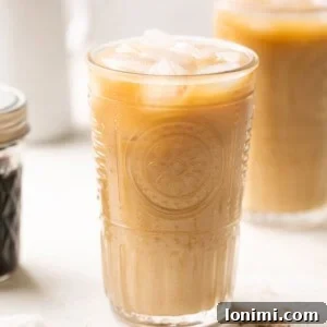 A glass of brown sugar shaken espresso with oat milk over ice, coffee beans, and brown sugar syrup in the background.