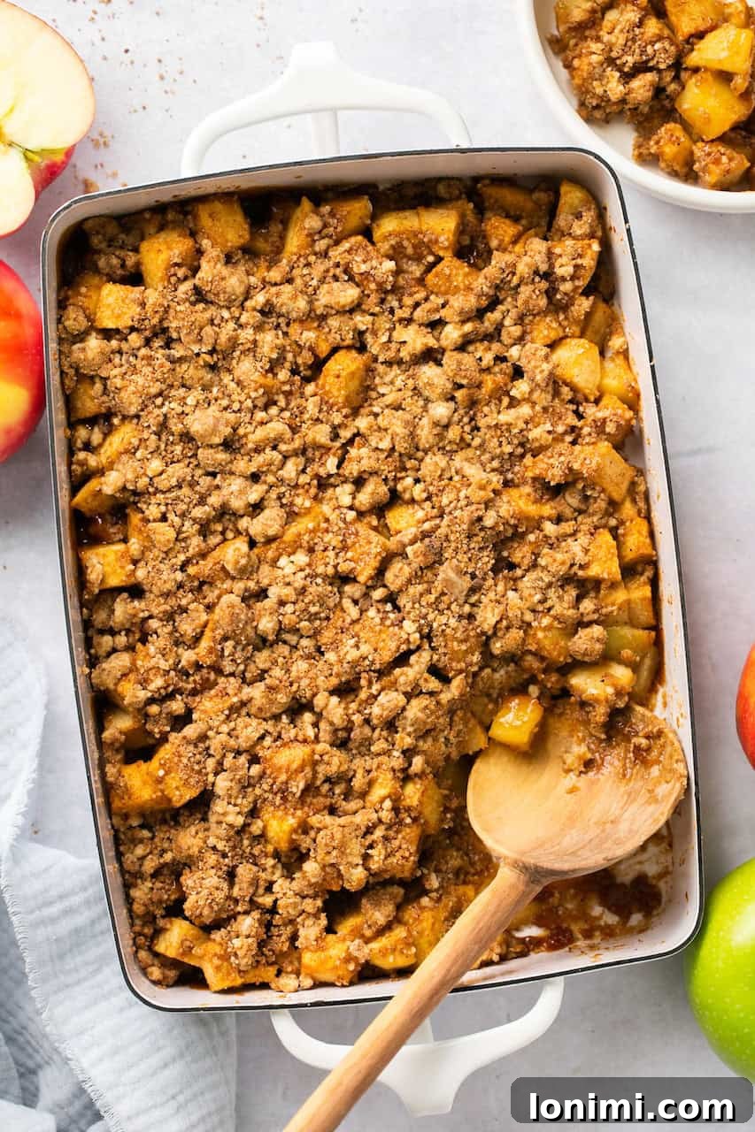 an overhead view of healthy apple crumble in a white casserole dish with a wooden spoon, ready to serve
