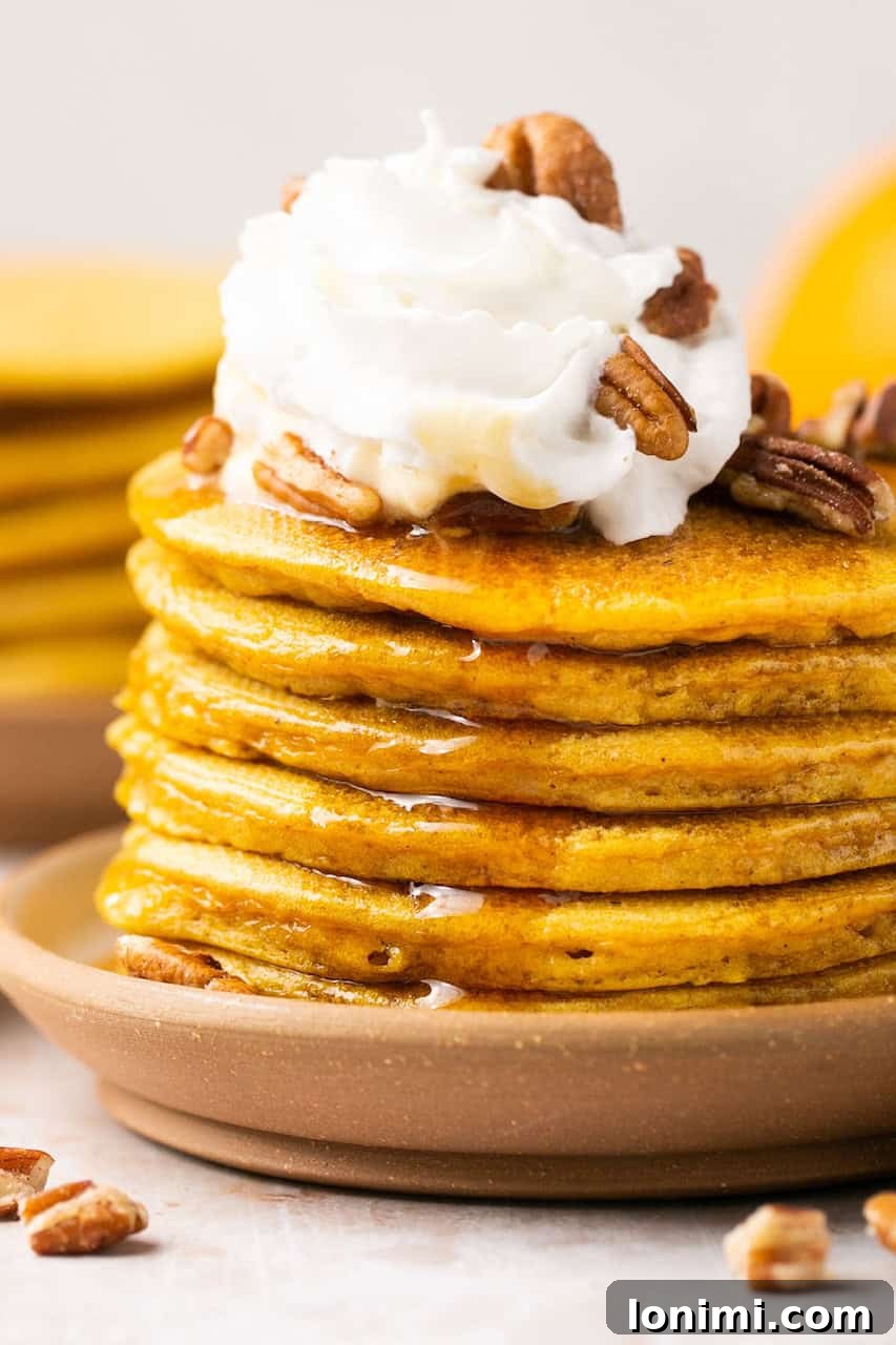 a close up of a stack of pancakes topped with whipped cream and pecans and syrup
