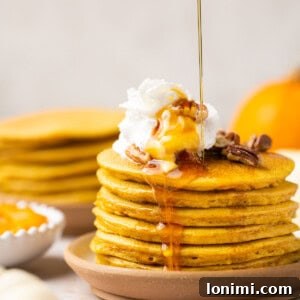 gluten free pumpkin pancakes stacked on a plate topped with pecans, whipped cream, and maple syrup