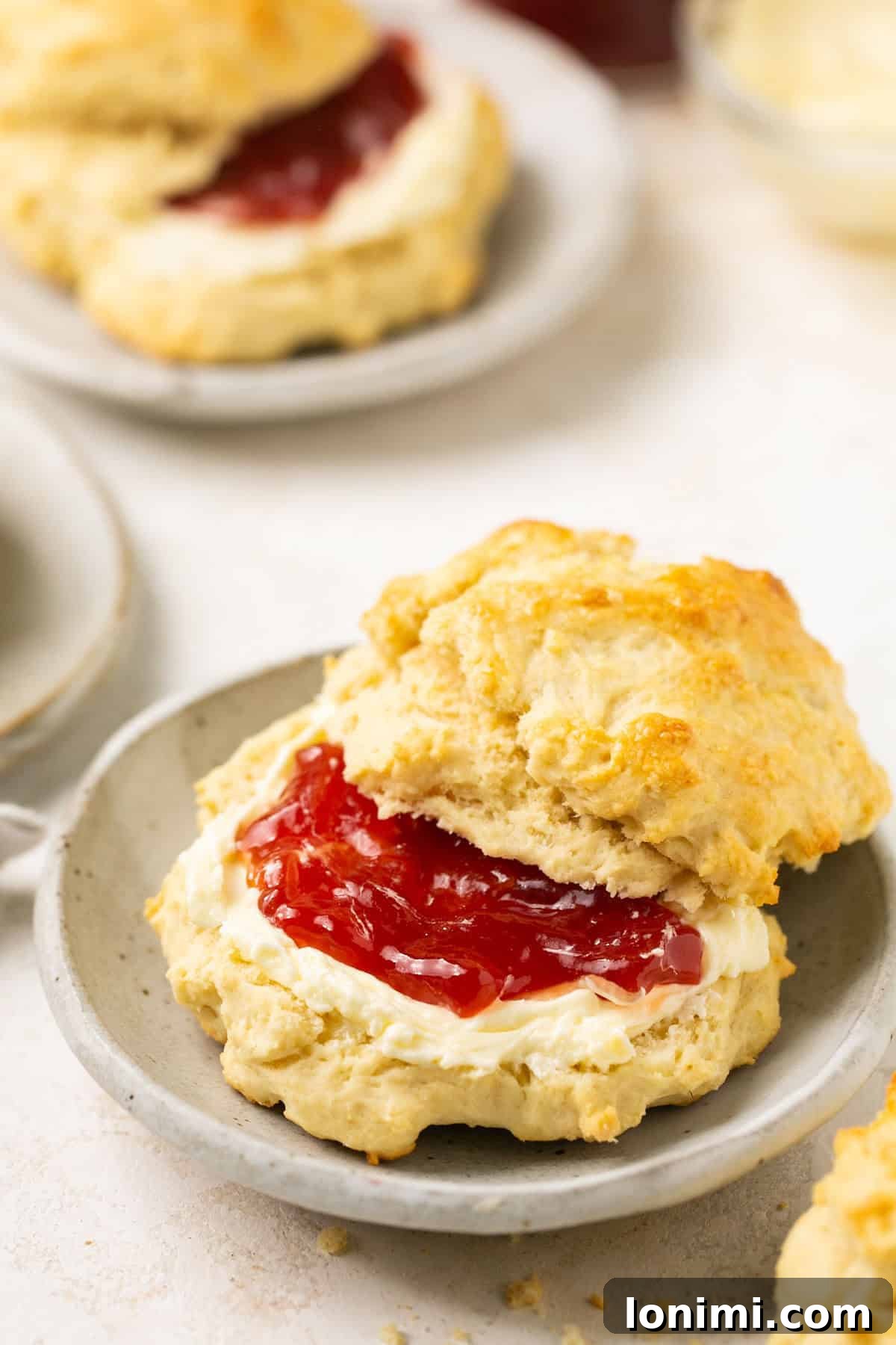 a gluten-free biscuit cut in half on a gray plate, revealing its fluffy interior, with butter and jam spread in the middle