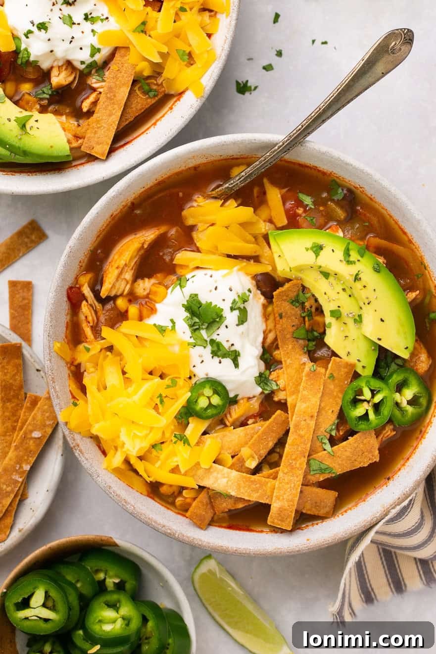 Chick-fil-A Inspired Tortilla Soup 2 An overhead shot of two white bowls filled with chicken tortilla soup and topped with homemade tortilla strips, avocado, sour cream, and shredded cheese.