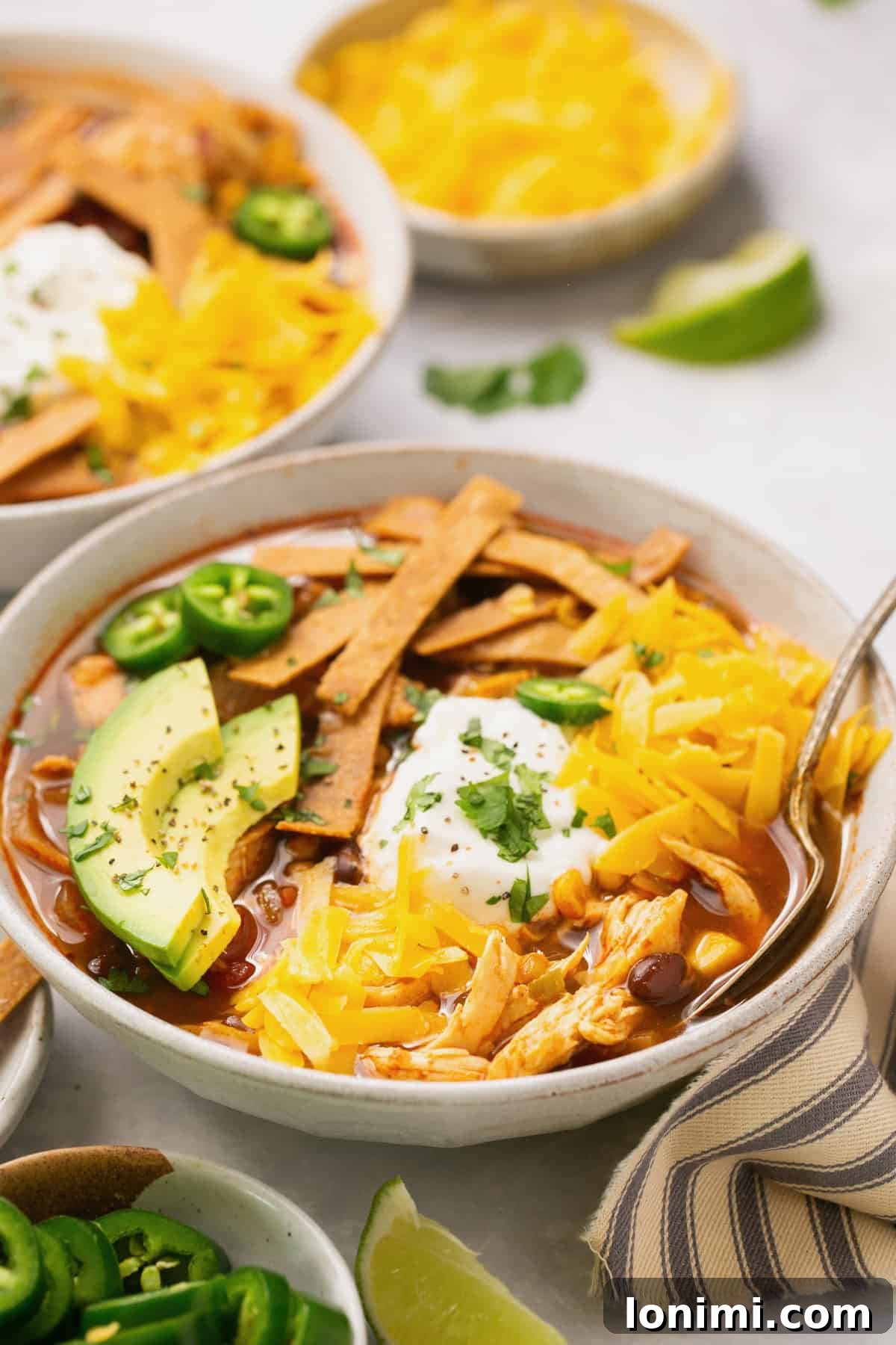 Chick-fil-A Inspired Tortilla Soup 7 A closeup shot of tortilla soup in a white bowl topped with avocado, cheese, sour cream, and cilantro