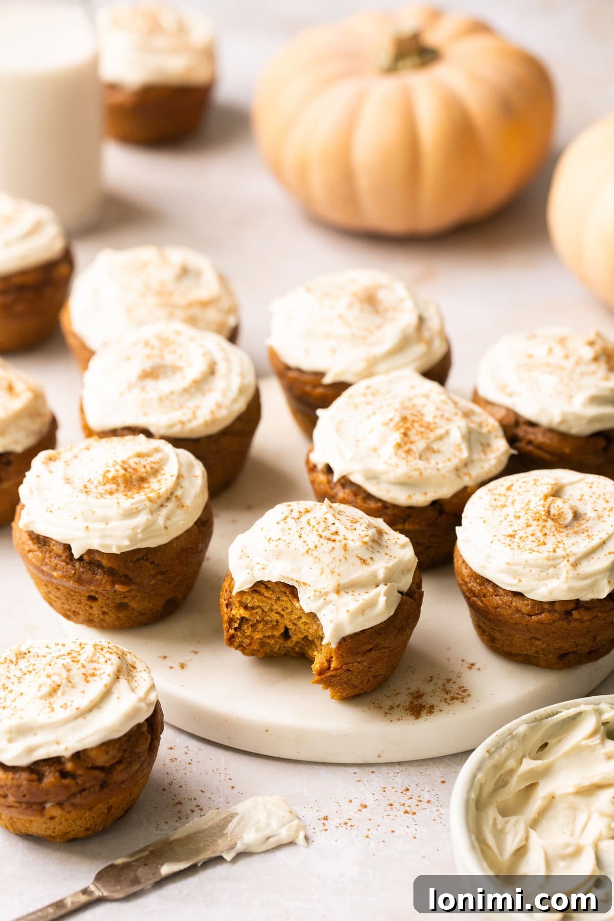 Simple Pumpkin Muffins with Velvety Dairy-Free Cream Cheese Frosting 7 Beautifully frosted pumpkin muffins arranged on a white tray, with one muffin showing a delightful bite taken out of it.