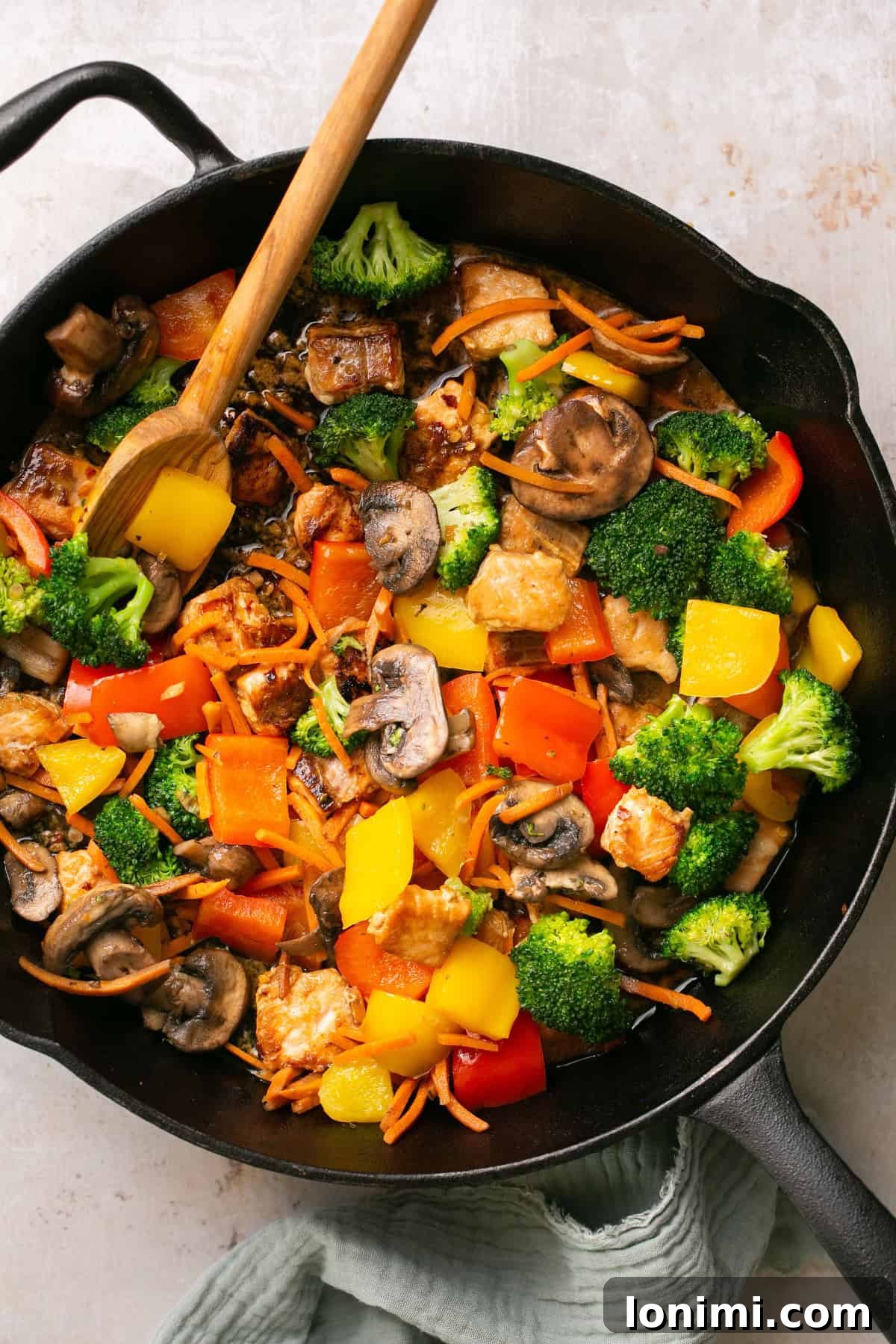 Effortless 30-Minute Gluten-Free Teriyaki Salmon Stir-Fry 6 A close-up shot of a cast iron pan containing salmon, mixed vegetables, and a rich stir fry sauce, with a wooden spoon resting in it.