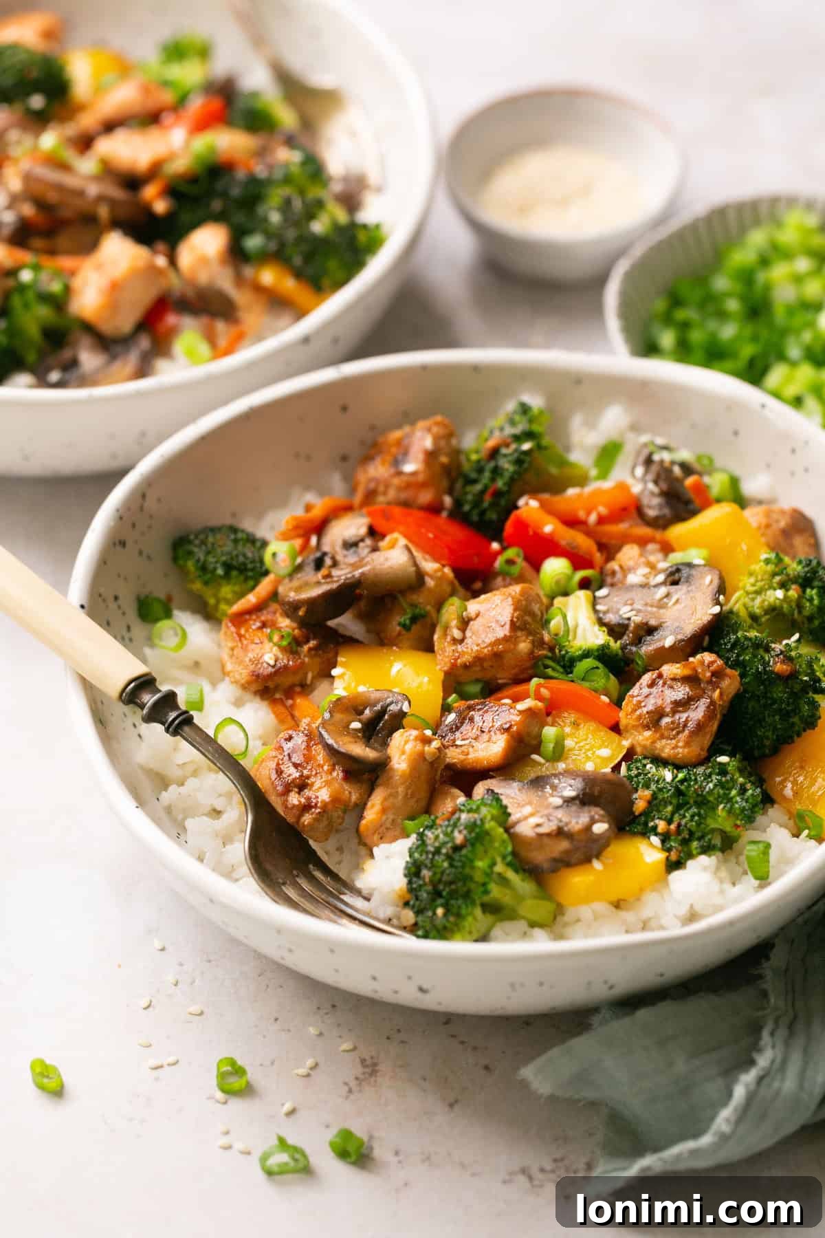 Effortless 30-Minute Gluten-Free Teriyaki Salmon Stir-Fry 7 Two white bowls containing rice, salmon stir fry, and gluten-free teriyaki sauce with an ivory fork resting on the side of the bowl.