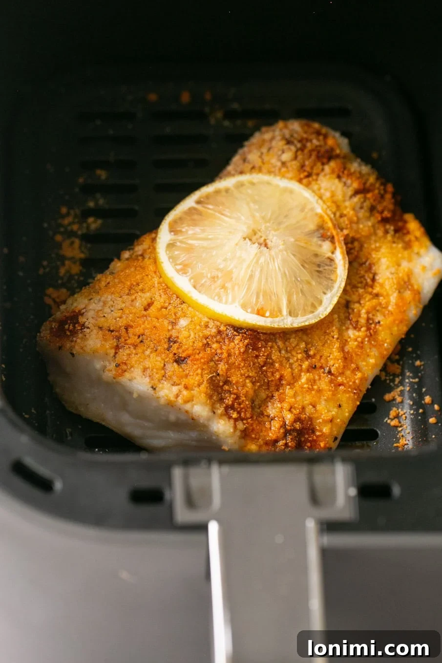 A photo of seasoned halibut with a lemon slice ready to be air fried in an air fryer basket.