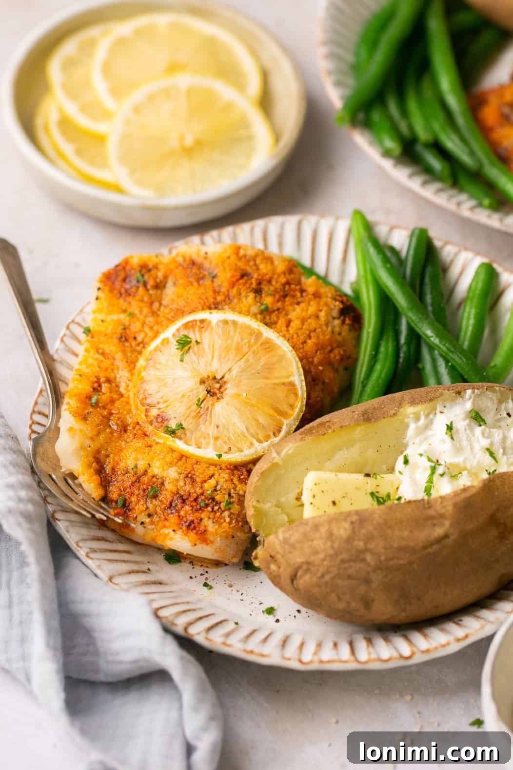 A close-up shot of a white plate with air fryer halibut next to green beans and a baked potato, highlighting the texture of the fish.