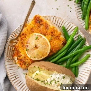 Air fryer halibut on a plate with green beans and a baked potato with butter and sour cream, a perfect weeknight meal.