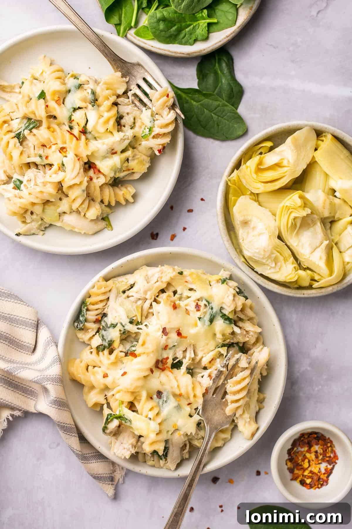 Spinach Artichoke Chicken Casserole Vegan Adaptable 6 Two plates generously filled with spinach artichoke chicken casserole, accompanied by a small bowl of fresh artichoke hearts.