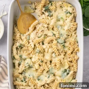 Spinach Artichoke Chicken Casserole Vegan Adaptable 8 Spinach artichoke chicken pasta bake in a casserole dish with a serving spoon taking a scoop out