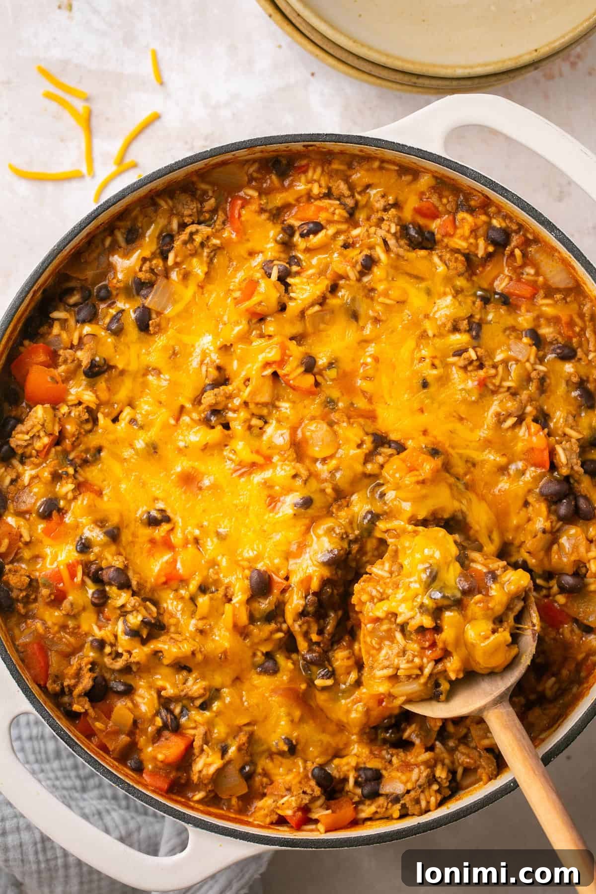 An overhead shot of the rich beef taco in a bowl recipe simmering in a large, deep skillet, with a generous layer of melted cheese bubbling on top, ready to be served.