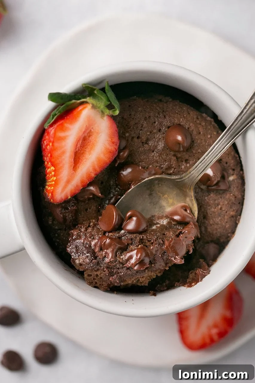 An inviting overhead shot of a perfectly baked chocolate protein mug cake in a white mug, garnished with a vibrant sliced strawberry.