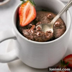 protein chocolate mug cake topped with chocolate chips and a strawberry slice with a spoonful being taken out