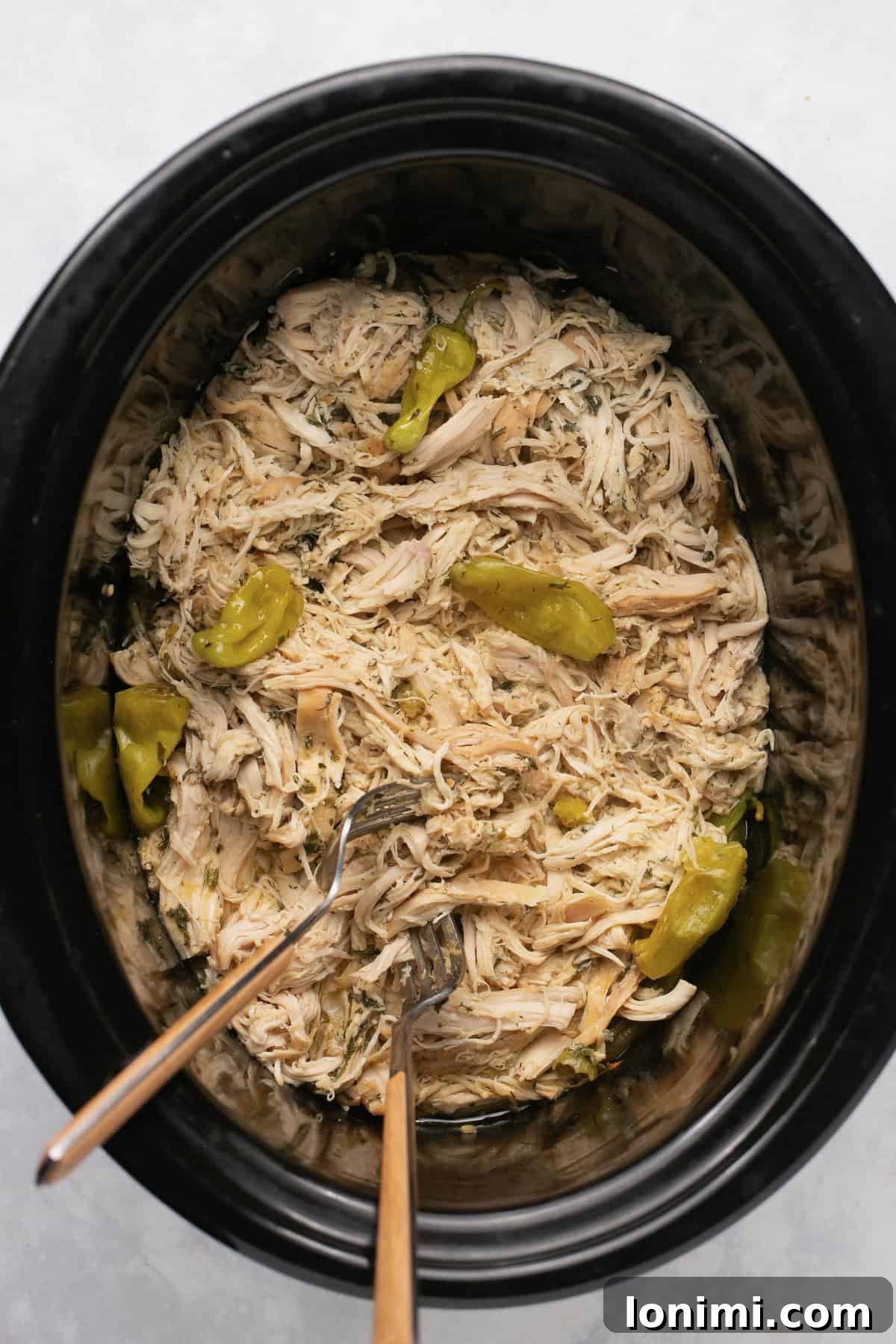 A slow cooker filled with bubbling Mississippi chicken, rich with spices and whole pepperoncini peppers, ready to be shredded.