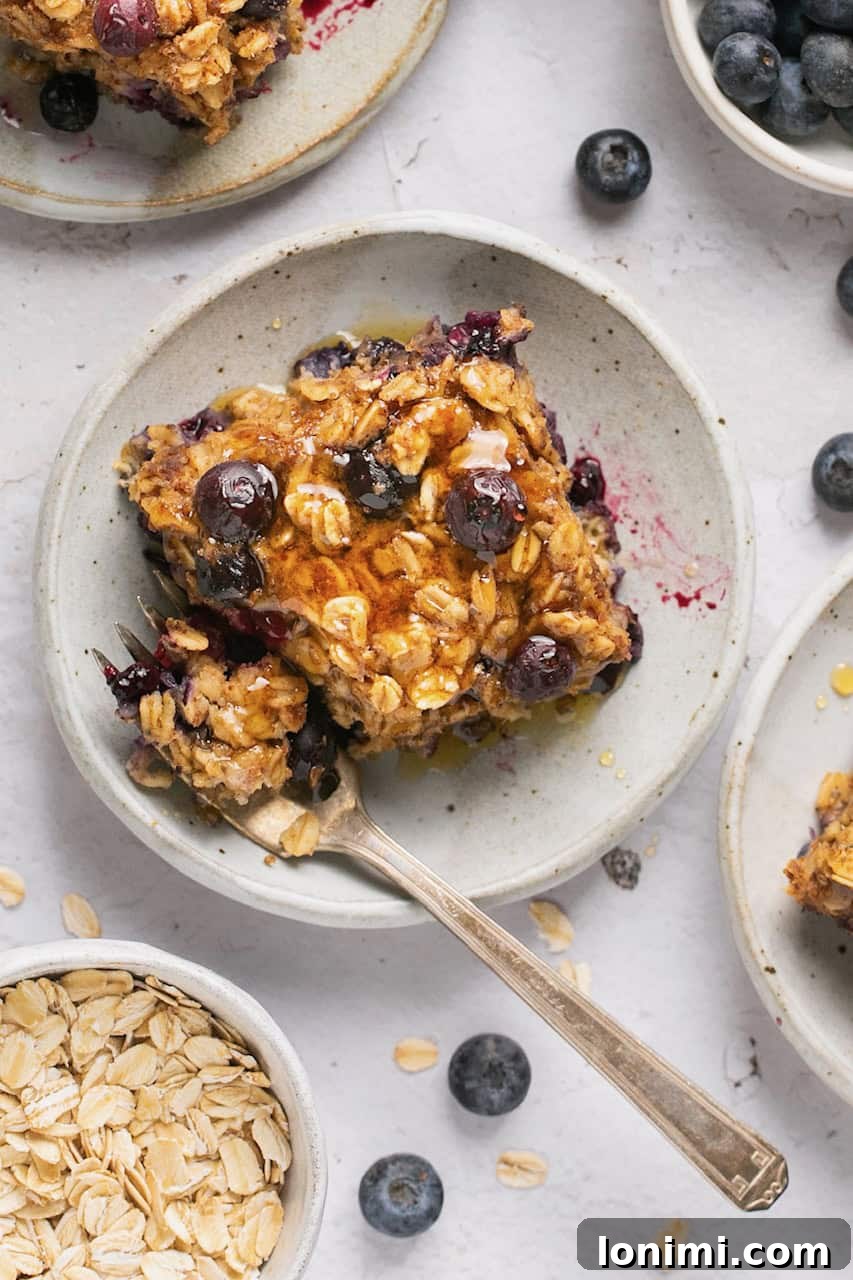 Protein-Packed Vegan Baked Oats 8 a close up of a sliced of baked oatmeal with blueberries and maple syrup on top