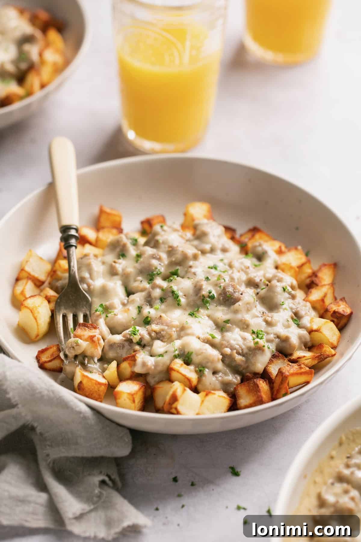 Effortless Keto Sausage Gravy 8 A hearty serving of keto sausage gravy and crispy potatoes in a white bowl, ready to be enjoyed with a fork.