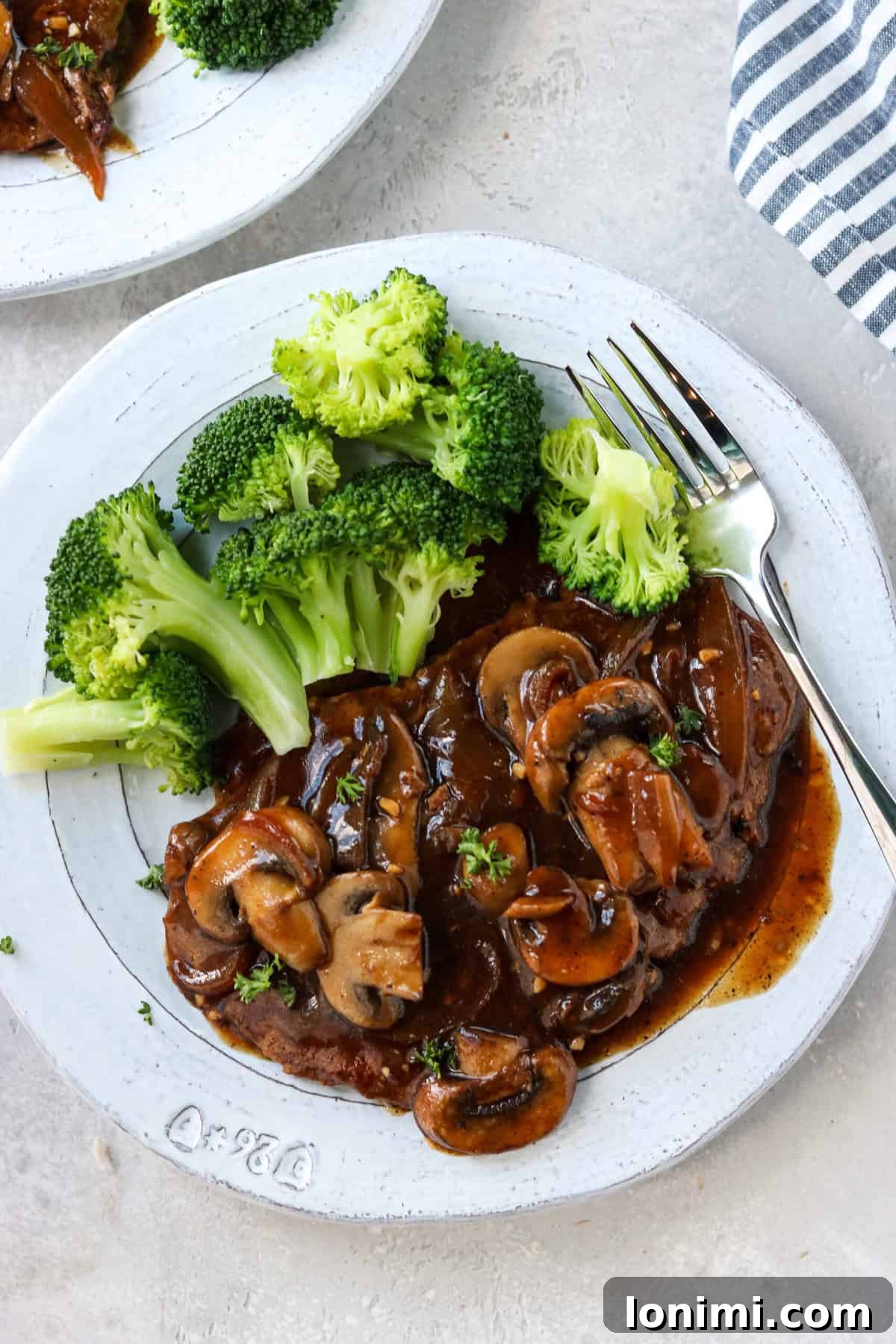 Effortless Tender Cube Steak 2 Cubed steak with mushrooms and onion gravy on a gray plate with steamed broccoli, showcasing a healthy and delicious meal.